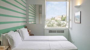 A bedroom with two beds, a window with a city view, a mirror, and a bedside table with a lamp. - Appartamento a Villa Montuoro by Wonderful Italy (Rapallo)
