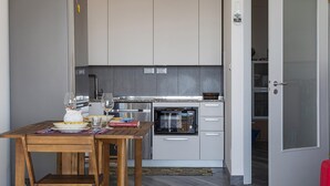 Kompakti keittiö, jossa on jääkaappi, mikroaaltouuni, uuni ja ruokapöytä tuoleineen.