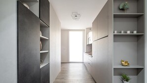 Een smalle gang met inbouwplanken aan beide zijden, een houten vloer en een deur aan het einde die naar een lichte kamer leidt.