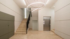Een modern interieur met een trap, een rond plafondlicht en een metalen liftdeur.