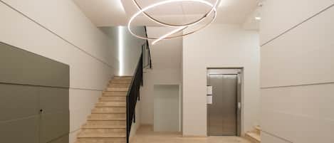 Ein modernes Interieur mit Treppe, einer wandmontierten runden Leuchte und einer Metall-Lift-Tür.