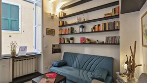 Una sala de estar acogedora con un sofá azul, una mesita de centro y una estantería llena de libros y objetos decorativos.