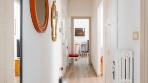 A hallway with a wooden floor, white walls, and a radiator. There are doors on both sides, and a mirror and a decorative item on the left wall. - Porta Mascarella Apartment by Wonderful Italy (Bologna)