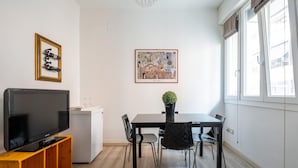 A modern living room with a flat-screen TV on a wooden stand, a dining table with chairs, a small refrigerator, and a framed artwork on the wall. - Porta Mascarella Apartment by Wonderful Italy (Bologna)