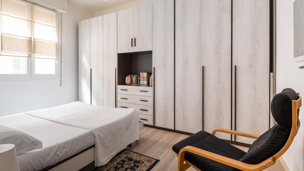 A bedroom with a bed, a chair, a wardrobe, and a window with blinds. - Porta Mascarella Apartment by Wonderful Italy (Bologna)