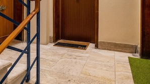 A hallway with a wooden door, a blue railing, and a green mat at the entrance. - Porta Mascarella Apartment by Wonderful Italy (Bologna)