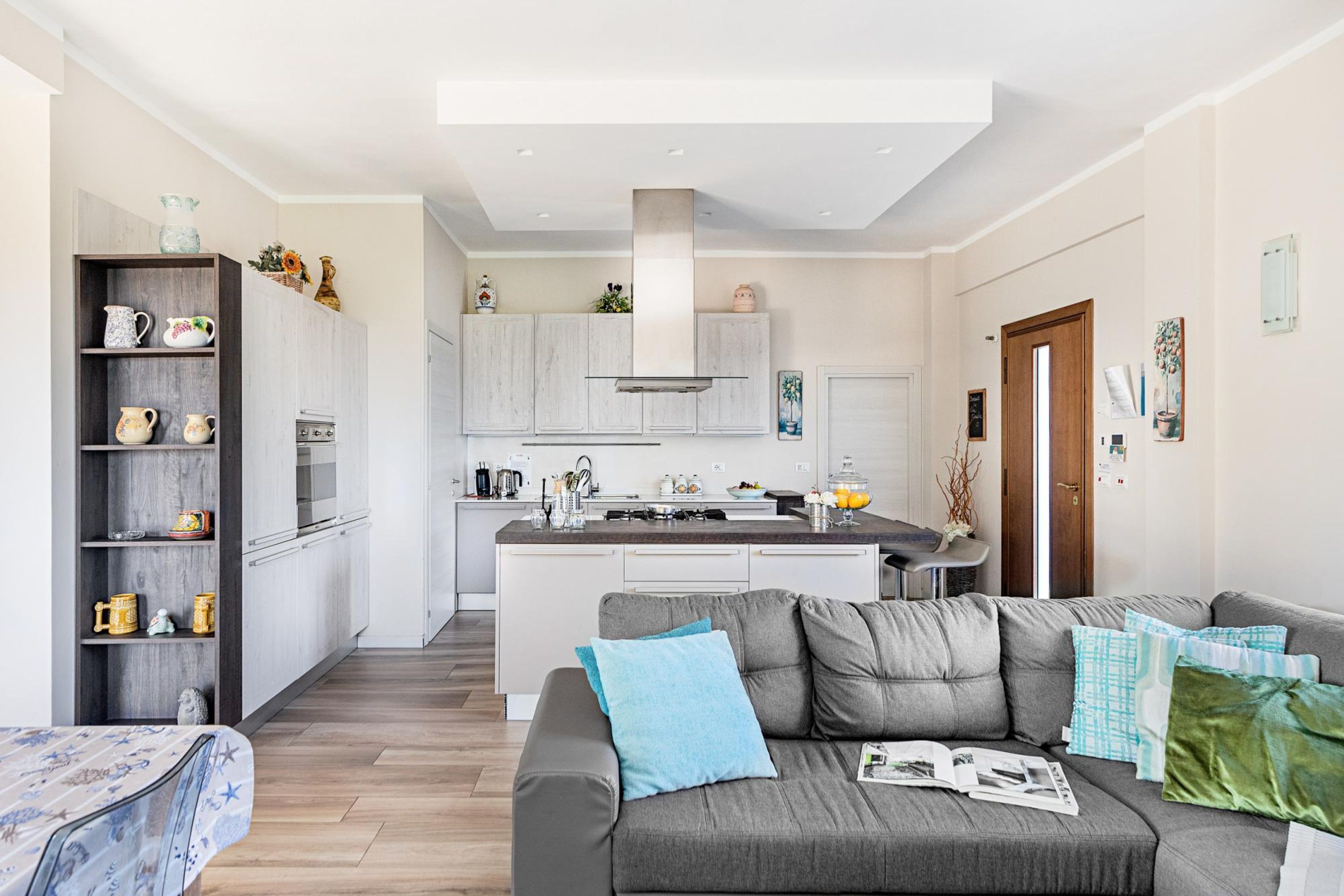 A modern kitchen with white cabinets, a central island, and a grey sofa in the living area.