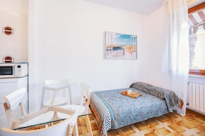 Een lichte, compacte kamer met een bed, een stoel, een tafel en een magnetron.