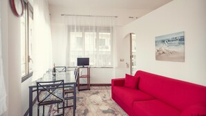 A living room with a red sofa, a dining table with chairs, a TV on a stand, and a large window with sheer curtains. - Sanremo Central Nest by Wonderful Italy (Sanremo)