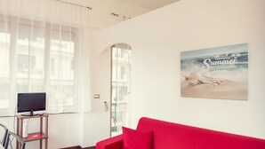 A room with a red sofa, a television on a stand, a window with sheer curtains, and a beach-themed poster on the wall. - Sanremo Central Nest by Wonderful Italy (Sanremo)