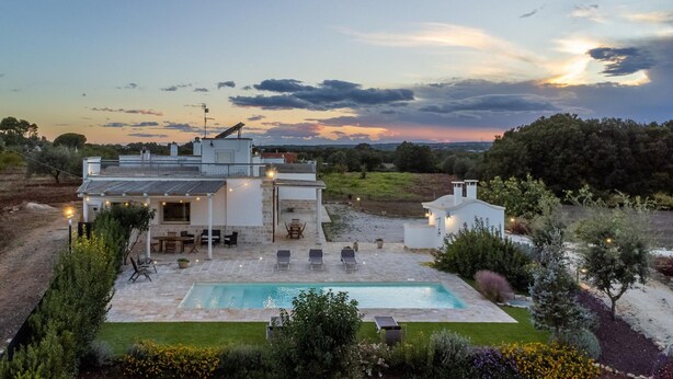 A modern house with a pool, outdoor seating, and a view of the sunset.