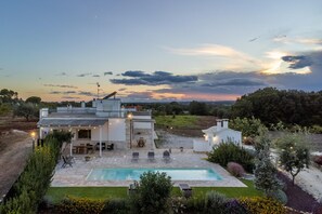 Une maison moderne avec une piscine, un espace salon extérieur et une vue sur le coucher de soleil.