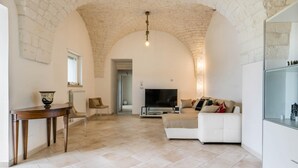A spacious living room with a stone ceiling, a white sofa, a TV, and a dining table with chairs.
