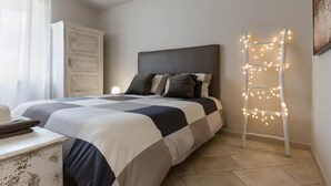A bedroom with a bed, a ladder with lights, a wardrobe, and a hat on a table.