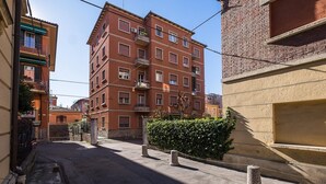 Eine schmale Straße mit einem rot backsteingefliesten Gebäude, einem verschlossenen Eingang und einer Hecke.