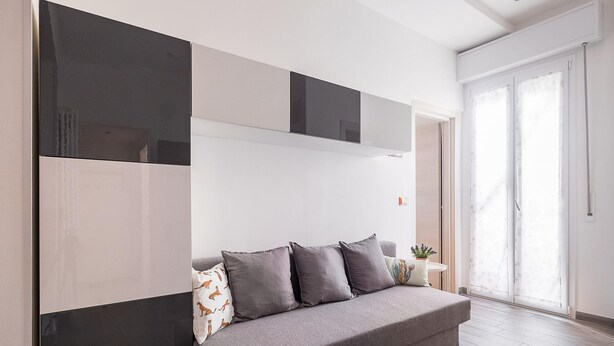 Ein modernes Wohnzimmer mit einem grauen Sofa, einem flachbildfernseher an der Wand und einer Glasschiebetür, die auf einen Balkon führt.