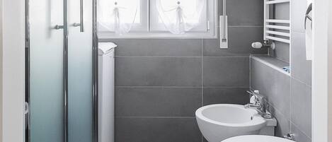 A modern bathroom with a shower, two toilets, and a window.