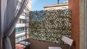 Ein Balkon mit einem Metallzaun, einem weißen Stuhl und einem kleinen Tisch mit orangefarbenen Kissen.