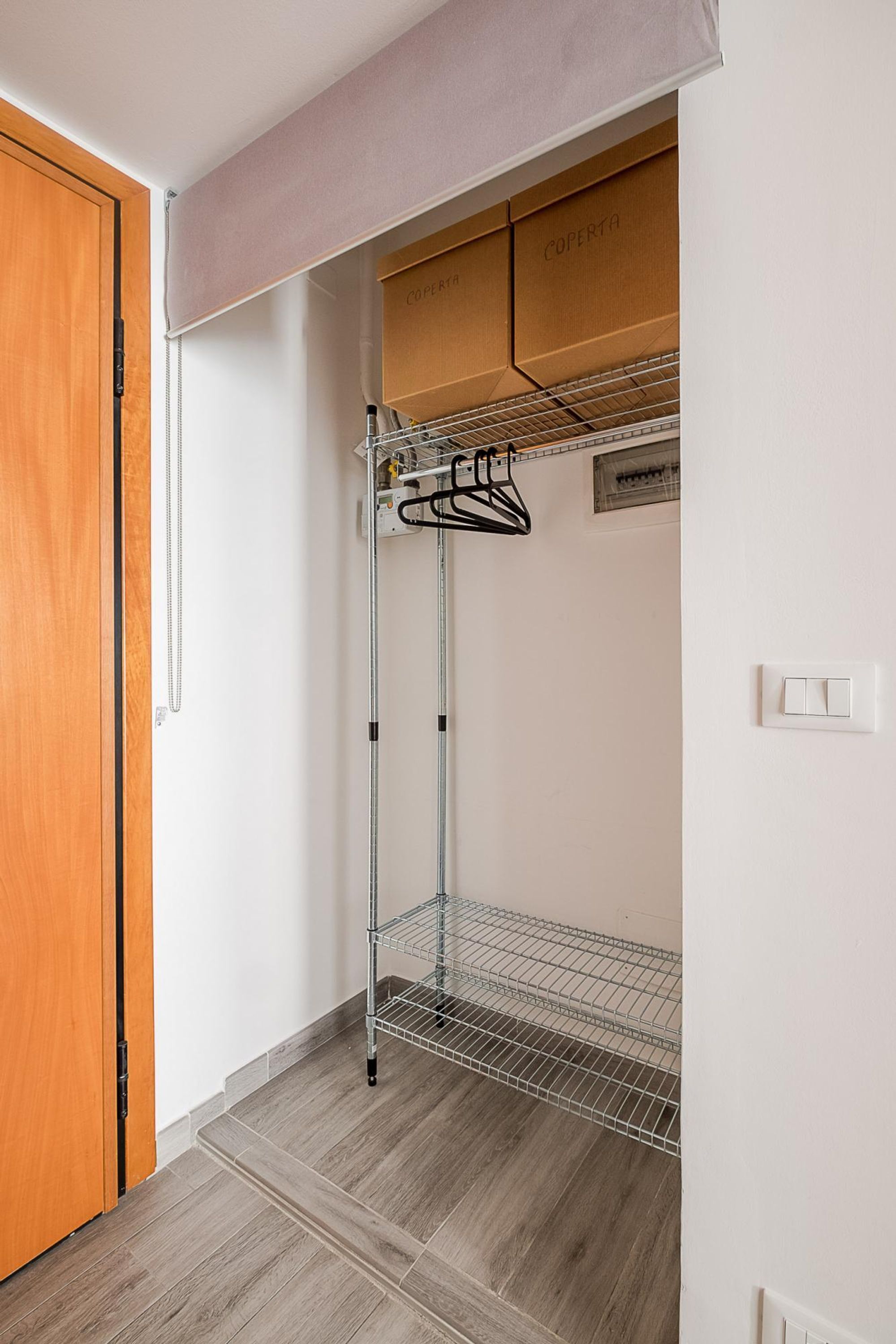A room with a wooden door, a metal rack, and a white wall with a light switch.