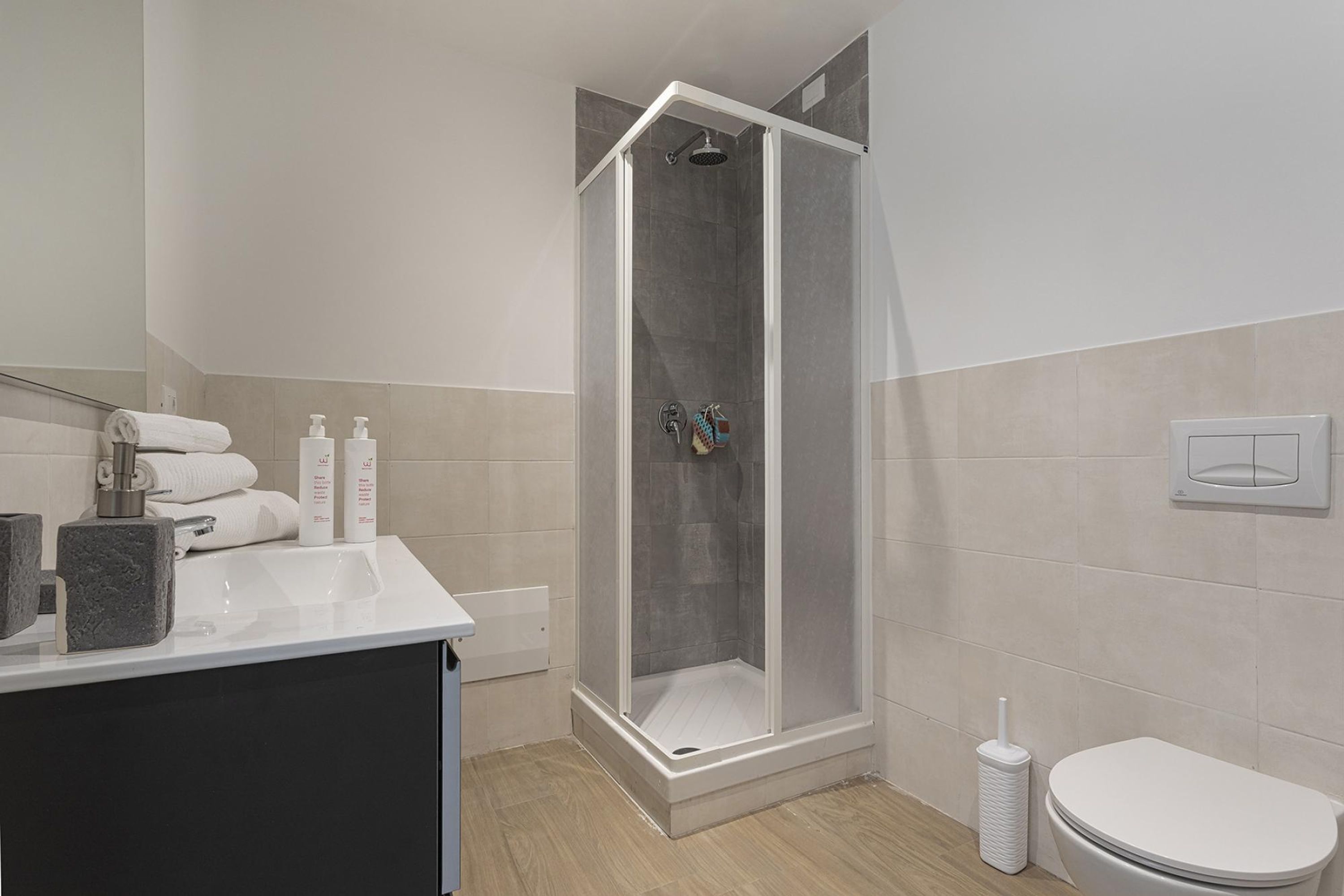 Et stilfuldt badeværelse med brusekabine, vask med toiletartikler og toilet.