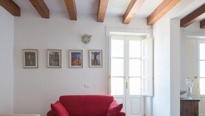 Une pièce avec une chaise rouge, des murs blancs, des poutres en bois et quatre œuvres d’art encadrées.