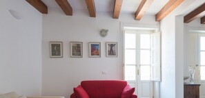 A room with a red chair, white walls, wooden beams, and four framed artworks.