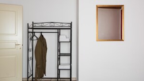 Une pièce avec un porte-manteau en métal sur lequel est accroché un manteau, une porte blanche et un tableau encadré au mur.