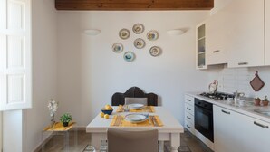 Une cuisine avec une table à manger pour deux personnes, des armoires blanches, une cuisinière et un luminaire suspendu.