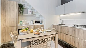 Una cuina moderna amb armaris blancs, un microones integrat i una cuina de gas. Hi ha una taula de dinar amb cadirees i un plat de fruita.