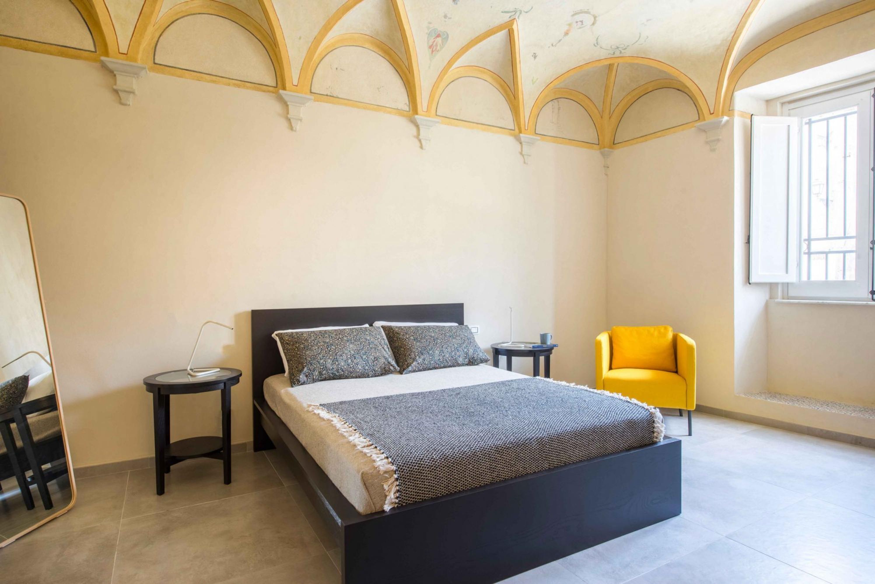 Un dormitorio con cama, mesita de noche, silla y ventana.