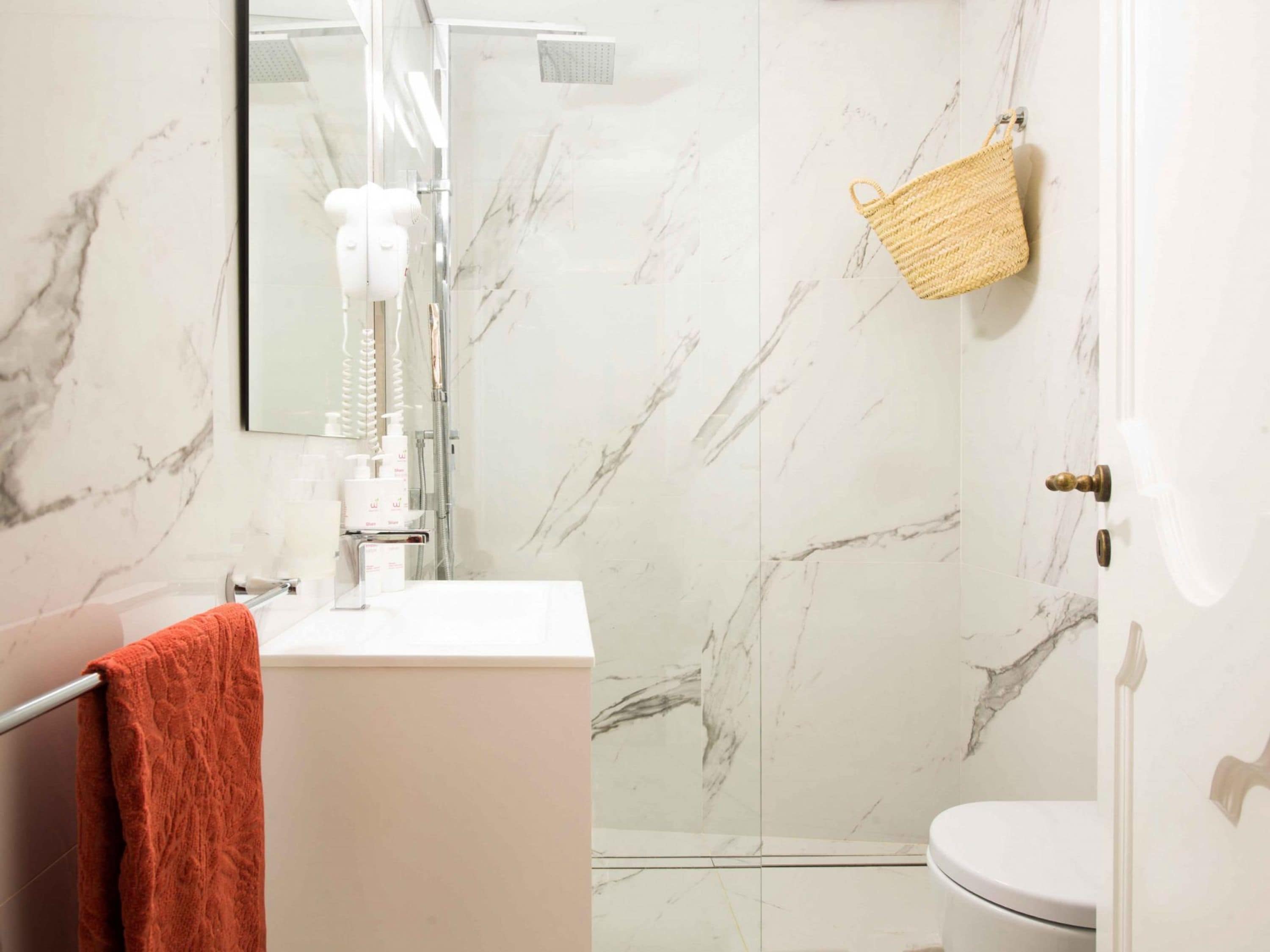 Un baño con un lavamanos blanco, una ducha con puerta de vidrio, un inodoro y un perchero con toalla.