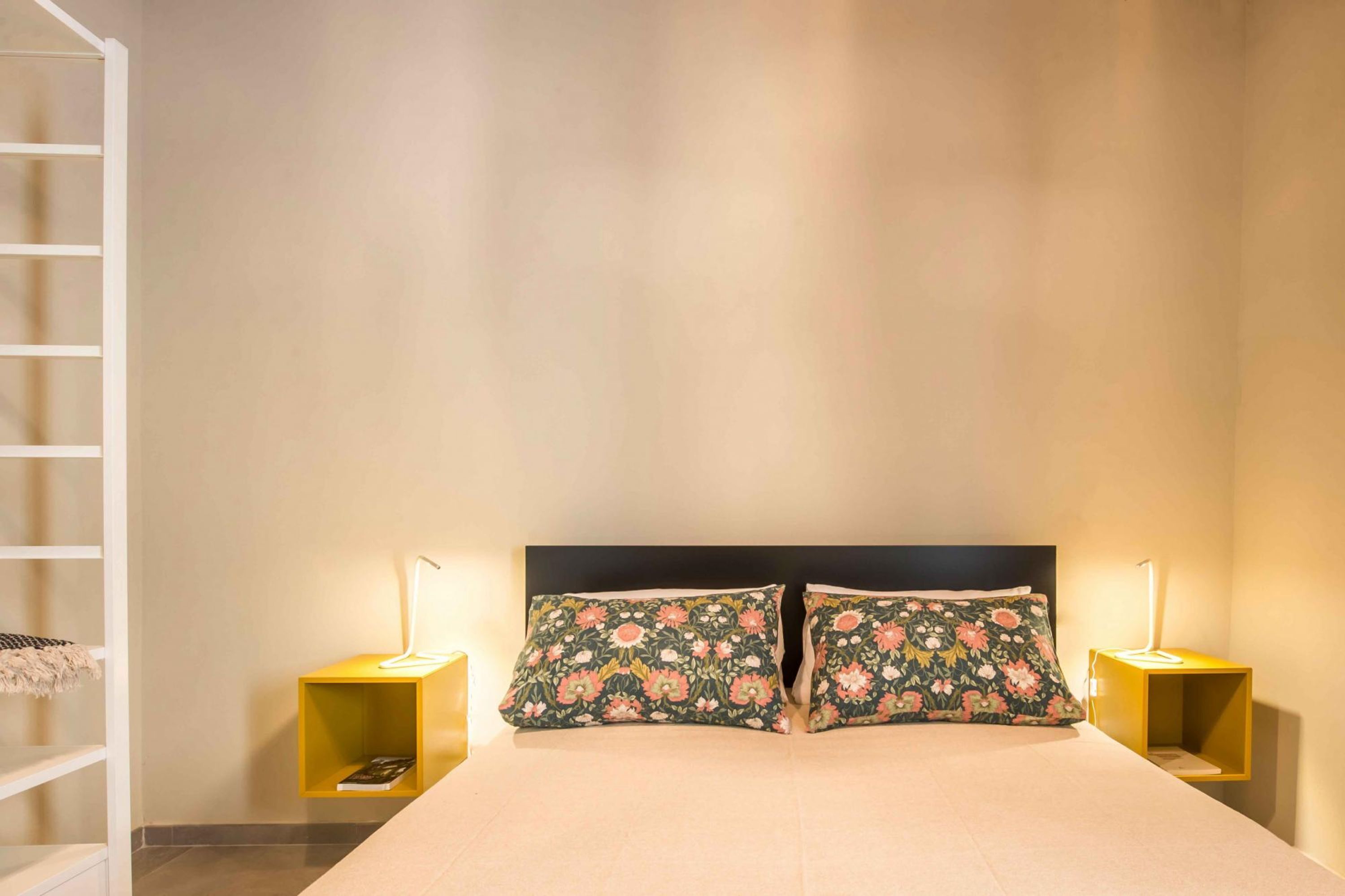 A neatly made bed with floral pillows, two bedside tables with lamps, and a white ladder against the wall.