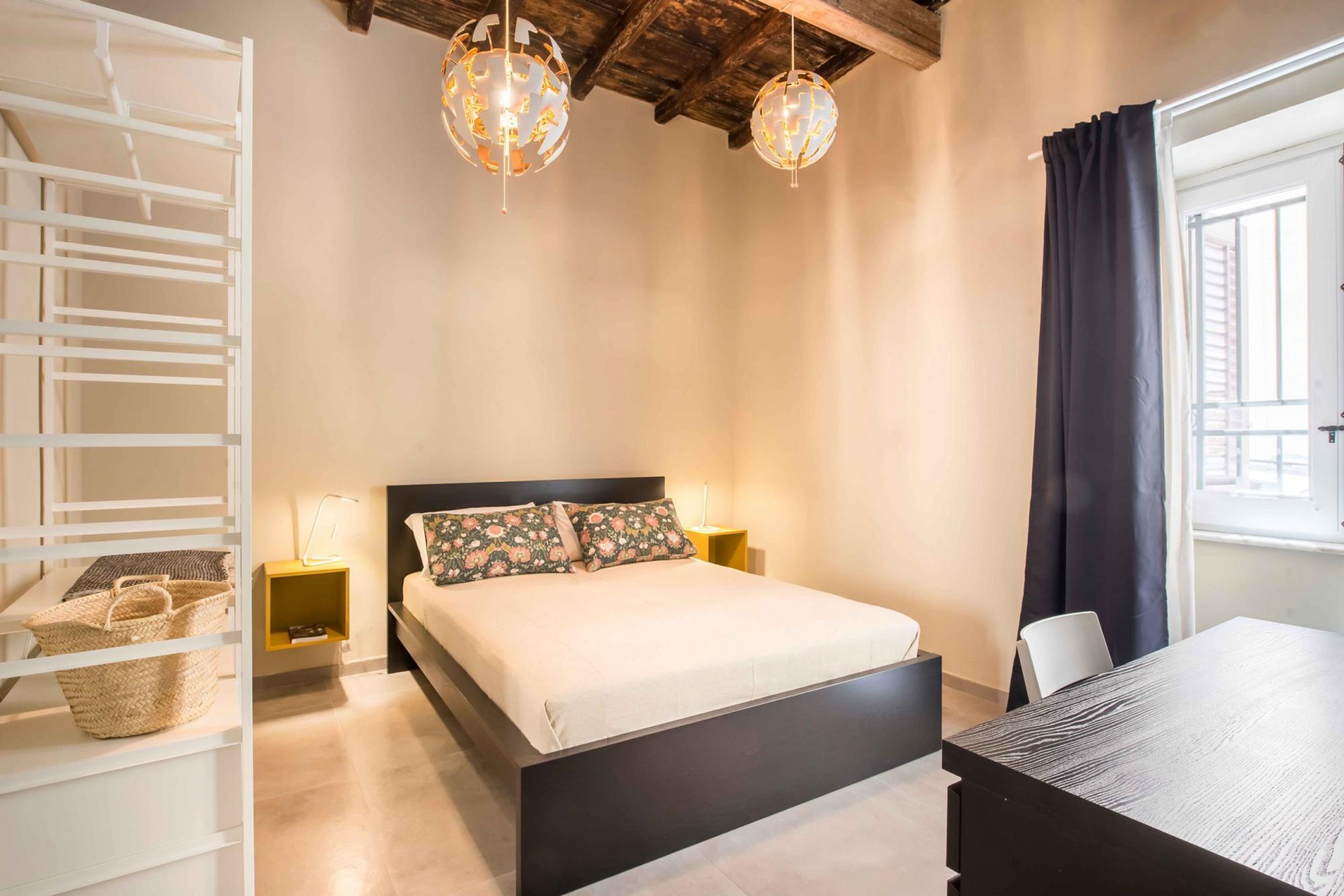 Un dormitorio con cama, lámparas de noche, cabecero de madera, escritorio y ventana con cortinas.