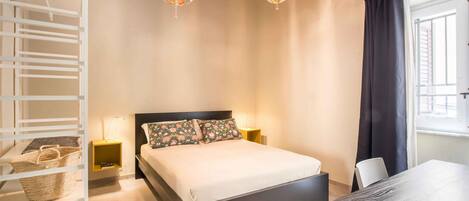 Un dormitorio con cama, lámparas de noche, cabecero de madera, escritorio y ventana con cortinas.