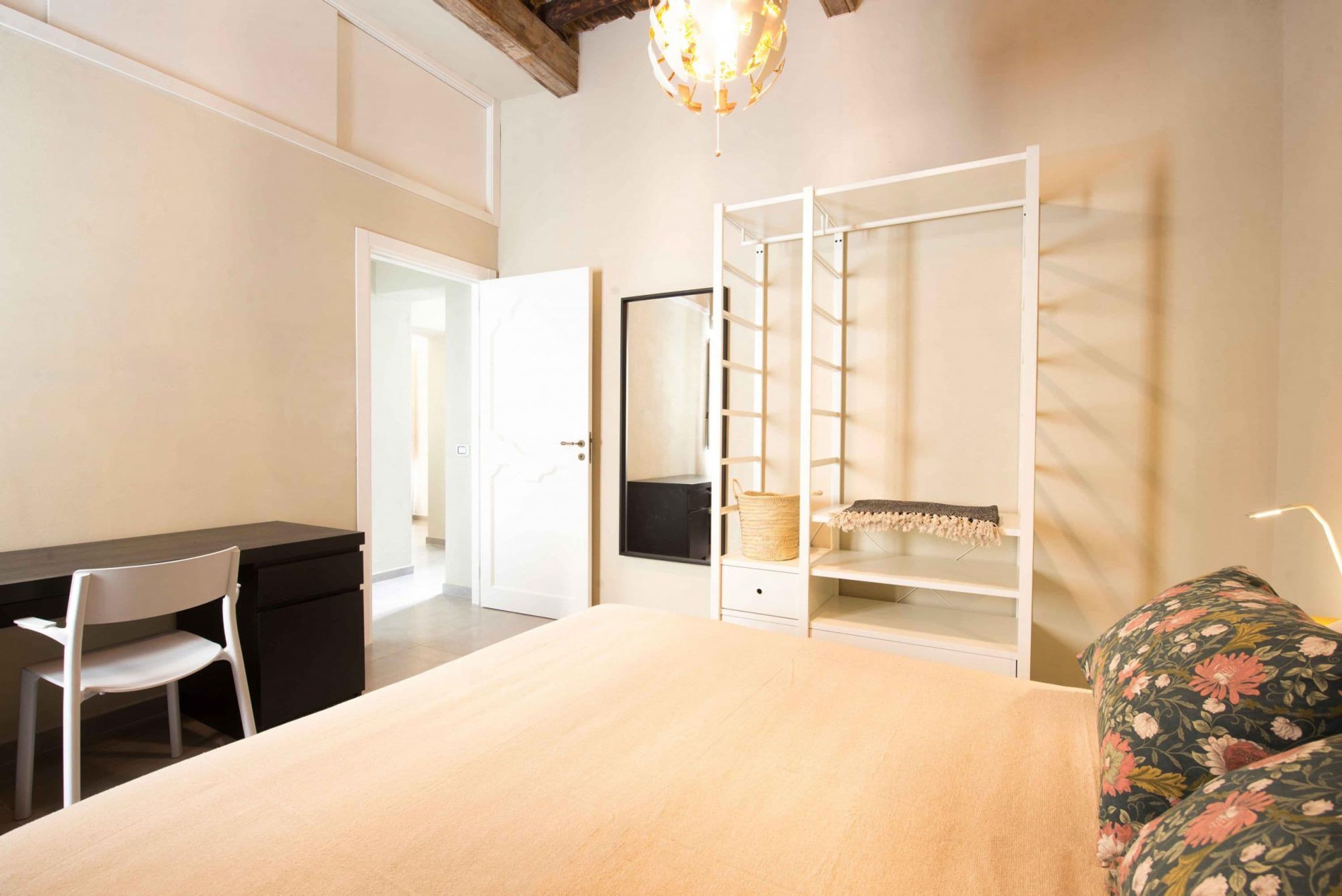 A bedroom with a bed, a desk, a chair, a wardrobe, and a hanging light fixture.