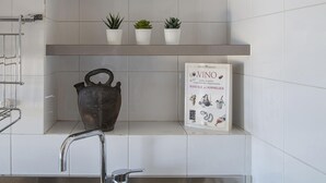 A kitchen with white tiles, a metal faucet, a shelf with three potted plants, a decorative metal pot, and a cookbook titled "VINO". - Casa Rosanna by Wonderful Italy (Genoa)