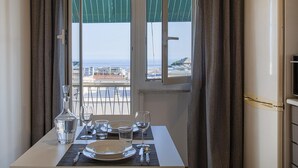 A dining table set with plates, glasses, and a decanter, positioned near a window with a view of the sea and buildings. - Casa Rosanna by Wonderful Italy (Genoa)