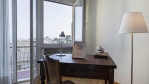 A room with a wooden desk, a lamp, a framed welcome sign, and a view of buildings through large windows. - Casa Rosanna by Wonderful Italy (Genoa)