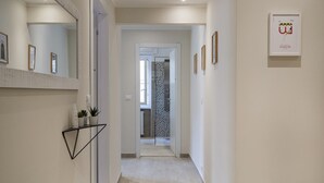 A hallway with a mirror, a shelf with plants, and framed pictures on the wall. - Carignano Design Apartment 7 by Wonderful Italy (Genoa)