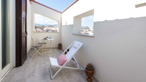Een balkon met een witte stoel, een klein tafeltje en een plant in pot.