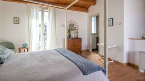 Een slaapkamer met een houten plafond, een bed met een grijze deken, een houten dressoir, een ronde spiegel en een raam met gordijnen.
