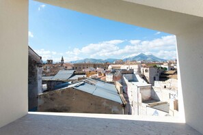 A view from a window overlooking a cityscape with buildings, a mountain in the background, and a clear sky.