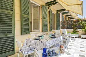 Un espace de restauration en plein air avec une table dressée pour deux personnes, entourée de chaises blanches ornées de motifs bleus.