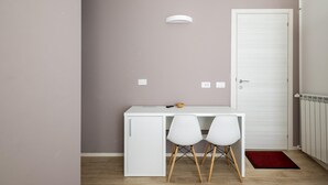 A small, neatly organized room with a white desk, two white chairs, a white door, and a red rug on the floor. - Cineteca White Studio by Wonderful Italy (Bologna)
