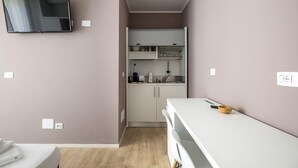 A compact room with a kitchenette, a flat-screen TV mounted on the wall, and a bed with a white cover. - Cineteca White Studio by Wonderful Italy (Bologna)