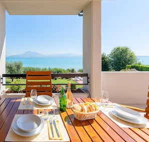 A wooden table set for dining with a view of the sea and mountains.
