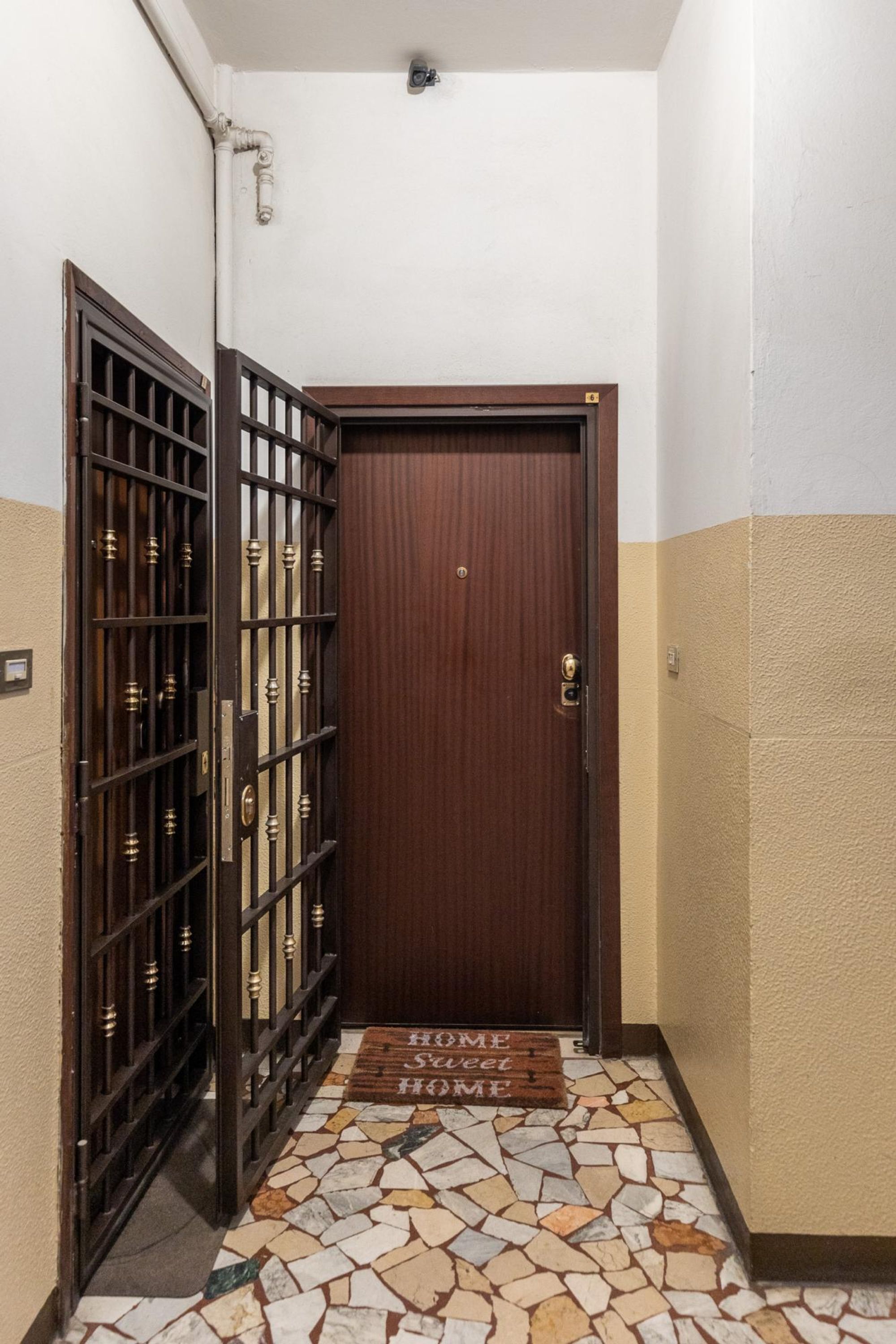 A hallway with a wooden door, a tiled floor, and a metal gate.
