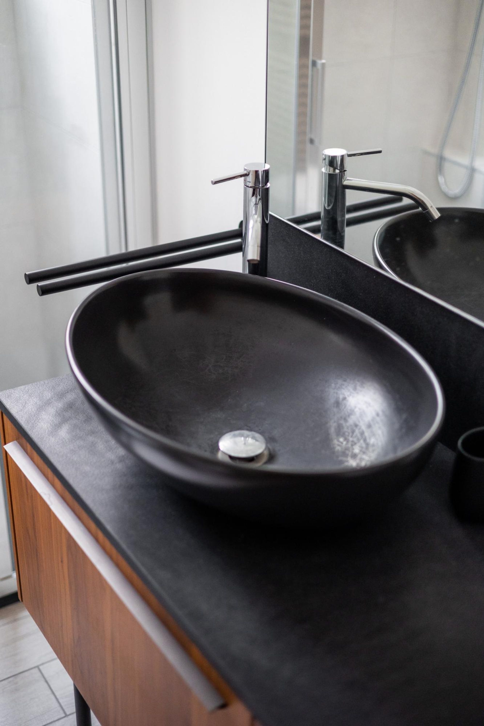 Un baño moderno con un lavamanos negro, un espejo y una zona de ducha.