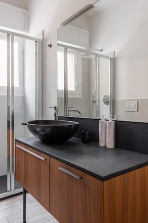 Een moderne badkamer met een grote zwarte wastafel, houten kastjes, een spiegel en twee shampoo flessen.