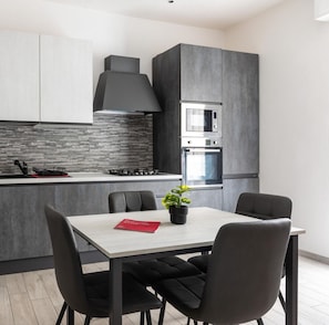 Een moderne keuken met een ingebouwde magnetron, oven en gasfornuis. Er staat een eettafel met vier stoelen en een potplant.